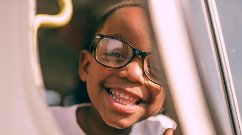 young child with glasses looking outside a car door