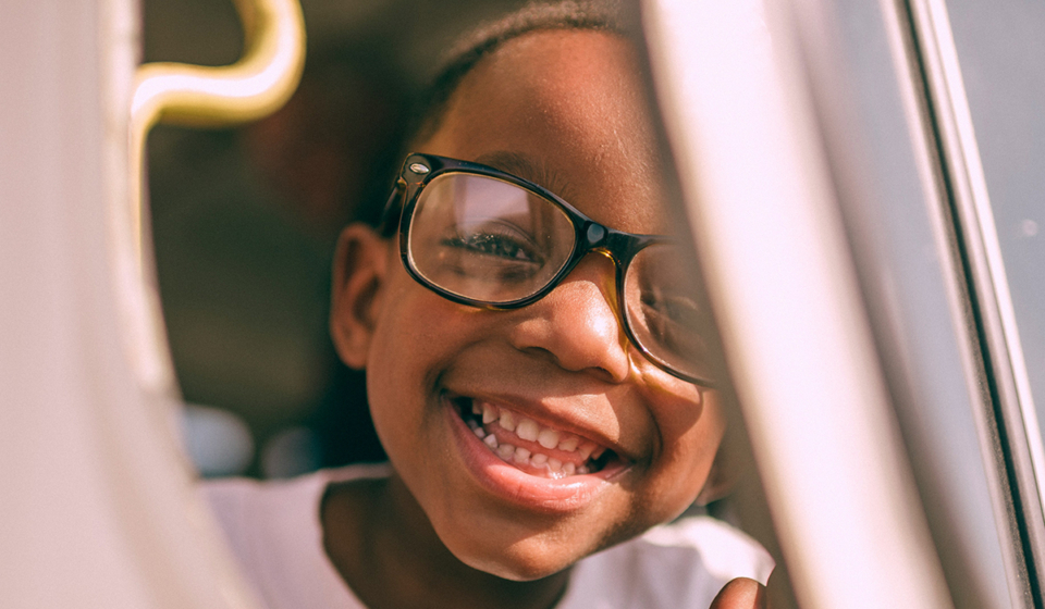 young child with glasses looking outside a car door