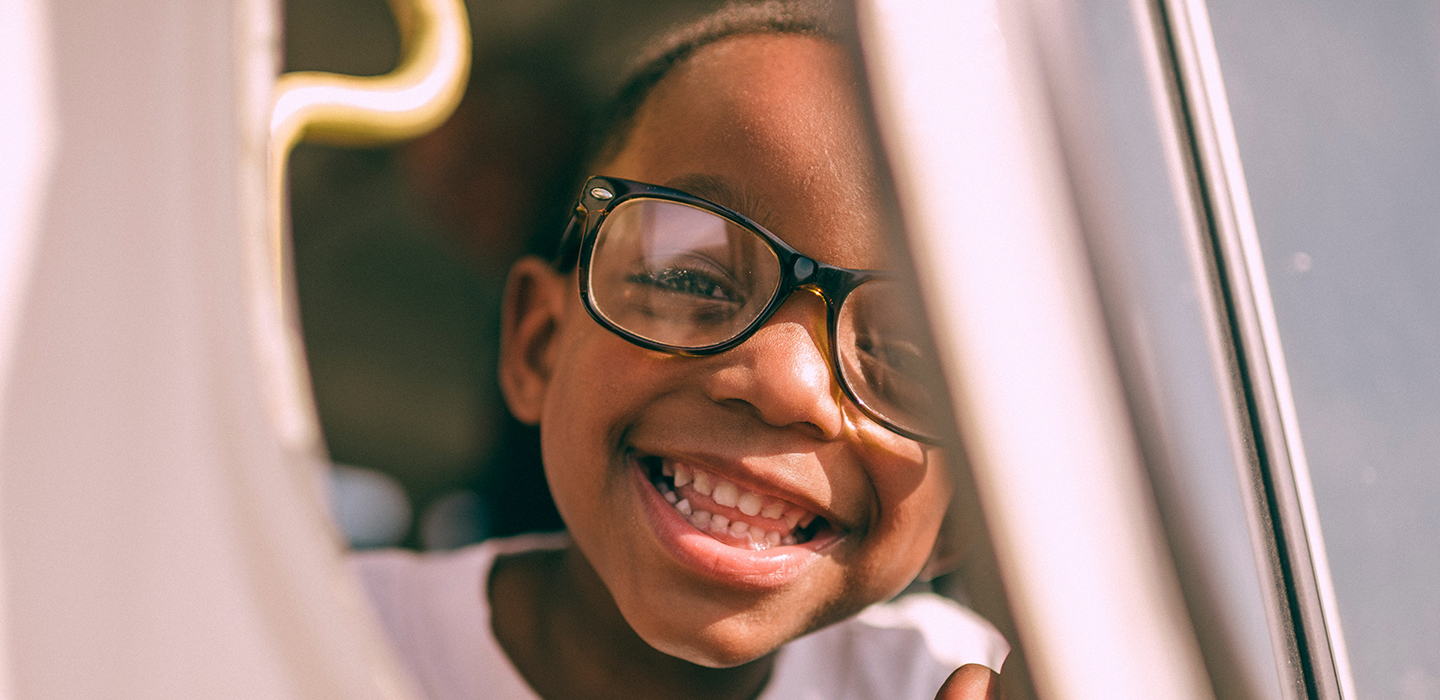 young child with glasses looking outside a car door