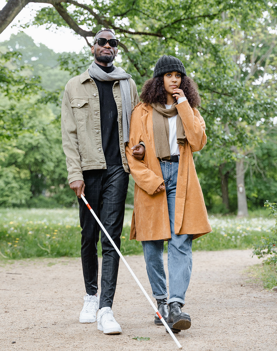 Couple walking in a park, the man is blind and the woman is helping with guiding him
